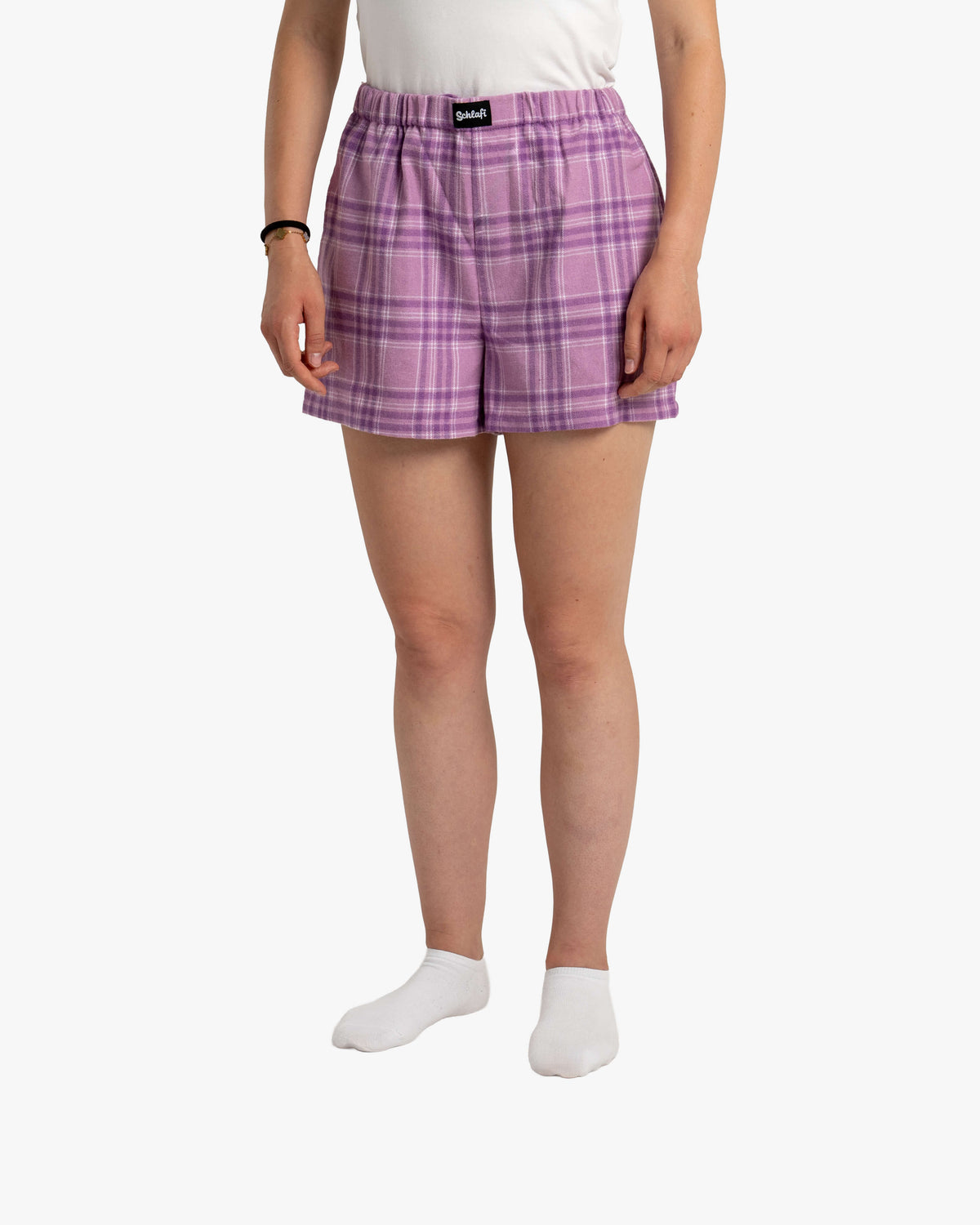 Nahaufnahme der Hot Pants in Wildberry, frontal getragen. Das violette Karomuster mit hell- und dunkel-lilanen Linien ist klar zu erkennen. Der Fokus liegt auf der Passform: locker geschnitten, mit elastischem Bund und mittlerer Beinlänge. Das SCHLAFI-Label ist mittig vorne aufgenäht.