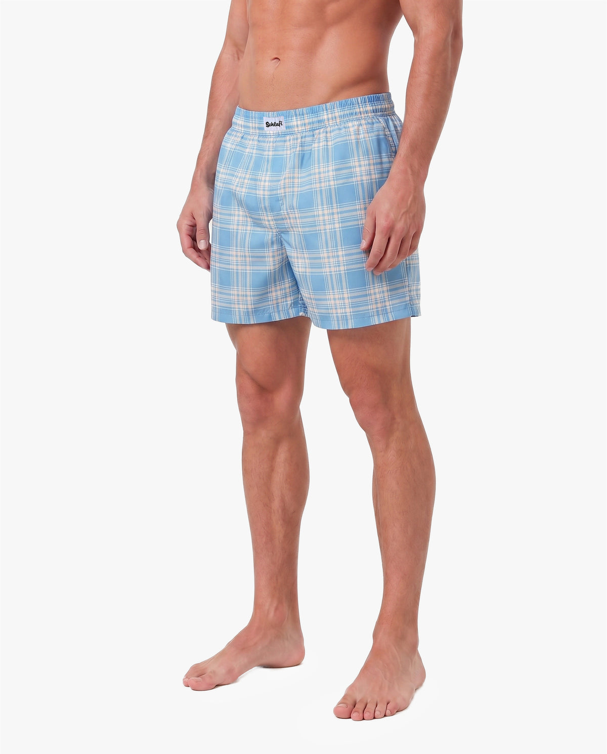 Alttext: Männliches Model trägt hellblaue Badeshorts mit weißem Karomuster. Die Shorts verfügen über einen elastischen Bund und eine lockere Passform. Freigestellte Produktaufnahme vor grauem Hintergrund.
