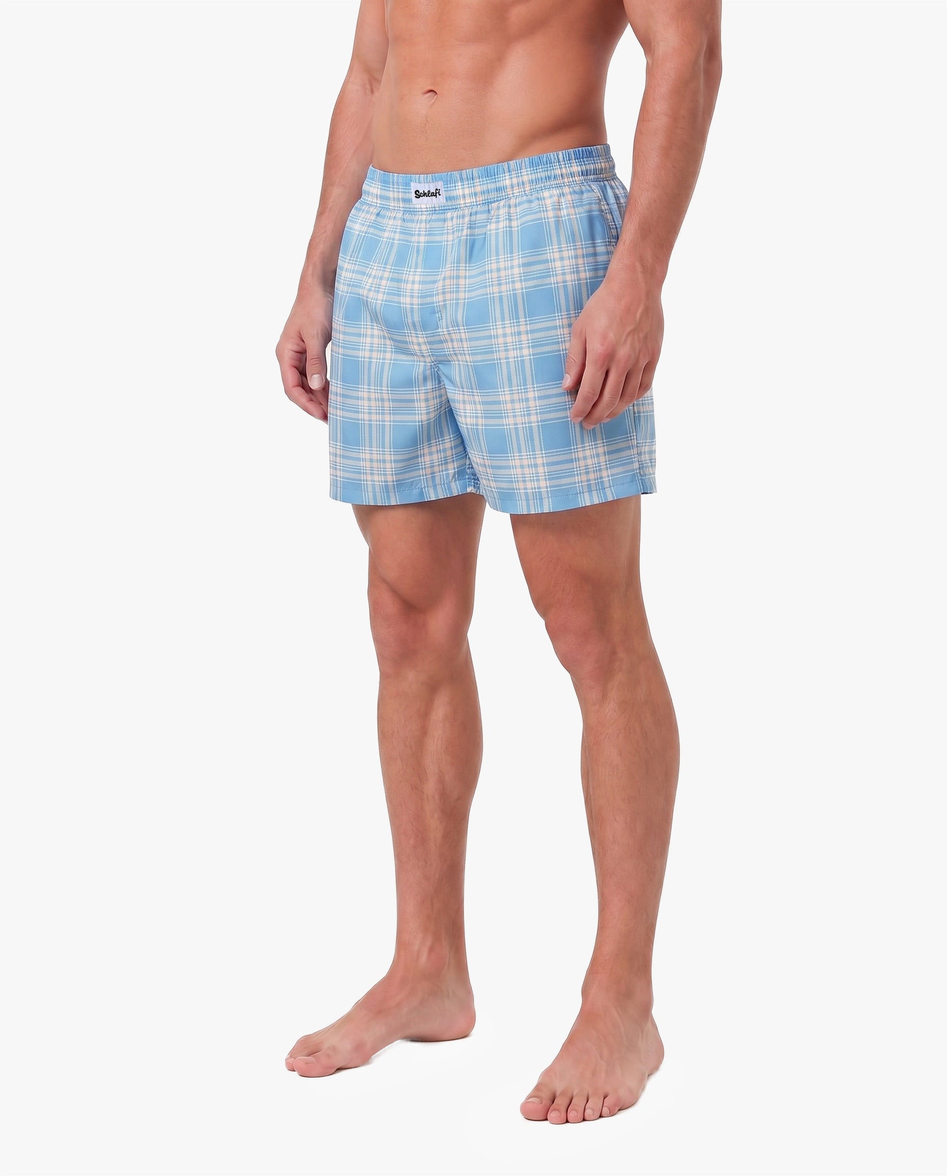 Alttext: Männliches Model trägt hellblaue Badeshorts mit weißem Karomuster. Die Shorts verfügen über einen elastischen Bund und eine lockere Passform. Freigestellte Produktaufnahme vor grauem Hintergrund.