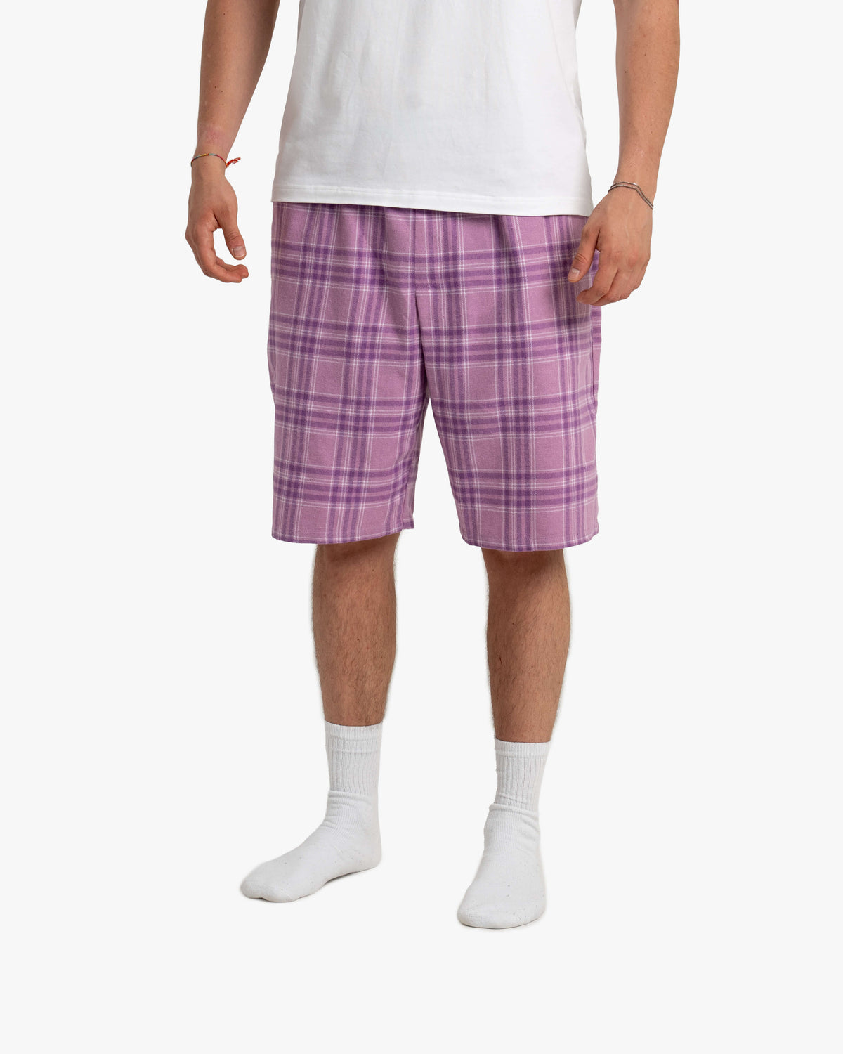 Mann steht frontal vor weißem Hintergrund und trägt die SCHLAFI Schorti in Wildberry – knielange, locker fallende Shorts mit dezentem Karomuster in hellen und dunklen Beerentönen, kombiniert mit weißem T-Shirt und Socken.